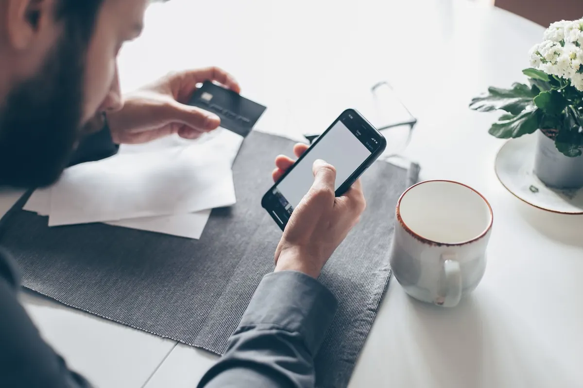 Muž s mobilem a platební kartou u stolu s kávou